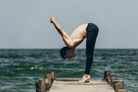 side view of shirtless man practicing yoga in uttanasana pose on pierの写真素材