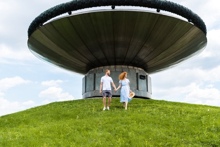 redhead couple holding hands and walking on grassy hill in front of modern building