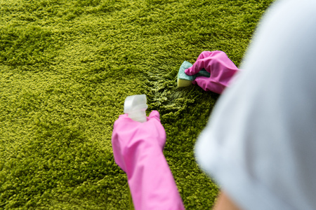 cropped shot of person in rubber gloves cleaning carpet with rag and detergent sprayの写真素材