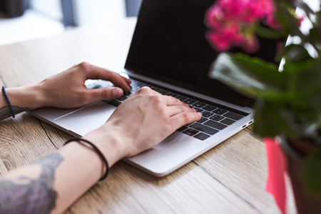 cropped image of woman with tattooed hands typing on laptop at table with flowersの写真素材