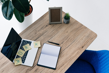 high angle view of laptop with blank screen, lettering work on post its, empty textbook, photo frame and potted plant on tableの写真素材