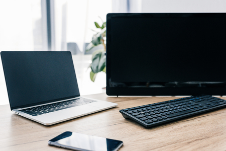 closeup view of smartphone with blank screen, laptop and computer at wooden tableの写真素材