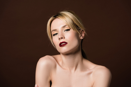 portrait of beautiful naked young blonde woman looking at camera isolated on brownの写真素材