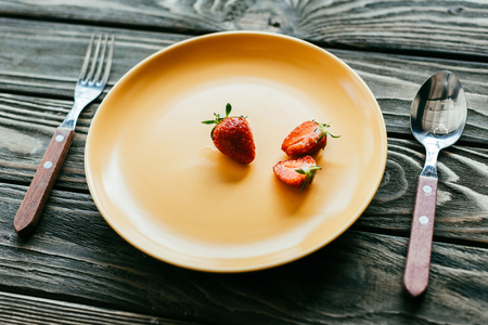Red strawberries served on plate with spoon and fork on wooden tableの写真素材