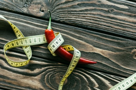 Red chili pepper with measuring tape on wooden tableの写真素材