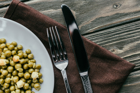 Fork and knife by plate with peas on textile napkin