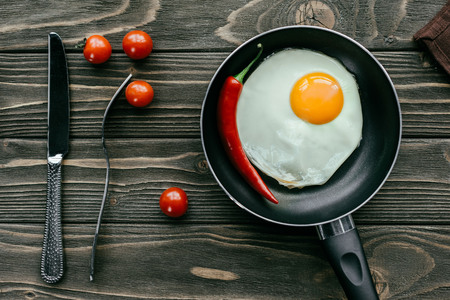 Fried egg in pan with tomatoes and cutlery on wooden tableの写真素材