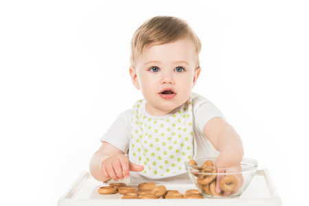 smiling baby boy eating bagels and sitting in highchair isolated on white backgroundの写真素材