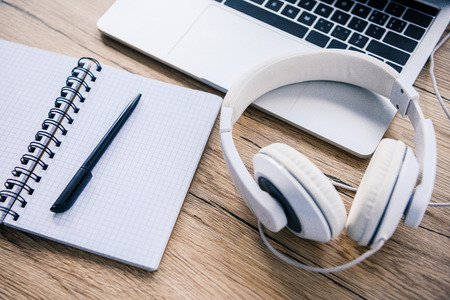 closeup view of headphones, empty textbook and laptop at wooden table