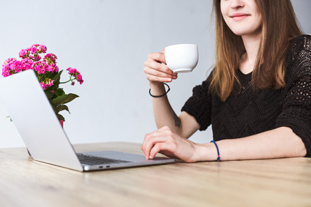 partial view of woman drinking coffee and using laptop at table with flowers