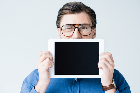 young man covering half of face with tablet with blank screen isolated on whiteの写真素材
