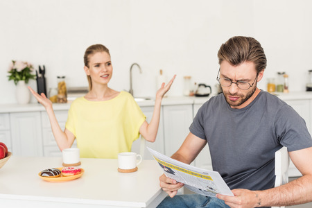 young woman with wide arms looking at boyfriend while he reading newspaper at table with breakfastの写真素材