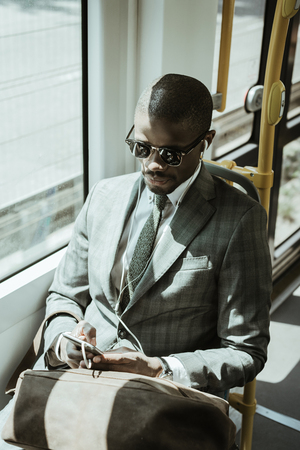 Young african american businessman listening to music while taking trainの写真素材