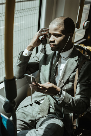 African american businessman wearing suit listening to music while going to work by trainの写真素材