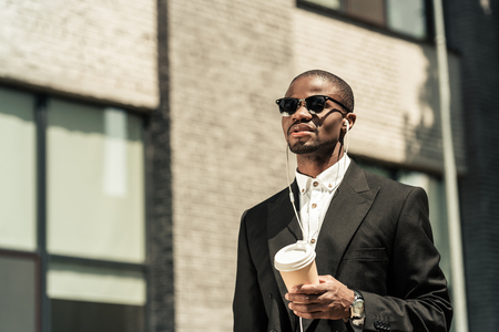Stylish man wearing suit listening to music and holding coffee cupの写真素材