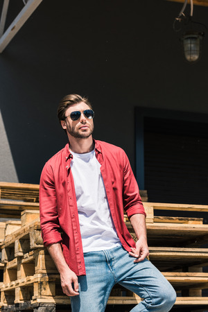 young stylish man in sunglasses posing near wooden palletsの写真素材