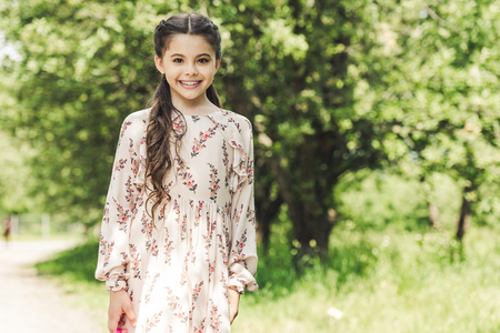 beautiful child in stylish dress looking at camera in summer parkの写真素材