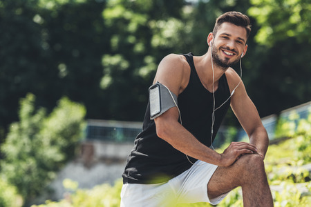 smiling sportsman in earphones with smartphone in running armband case doing exerciseの写真素材