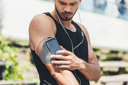 serious young sportsman in earphones with smartphone in running armband caseの写真素材