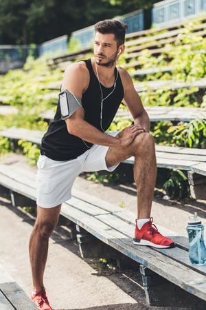 young sportsman in earphones with smartphone in running armband case doing exercise on bench at sport playgroundの写真素材