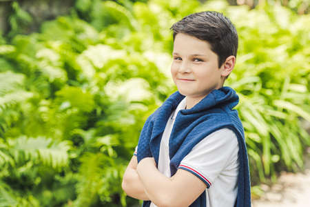 stylish kid with jumper over shoulders looking at camera with crossed armsの写真素材