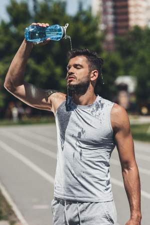 athletic young man pouring water on himself after trainingの写真素材