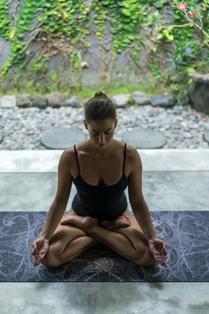 high angle view of young woman meditating in lotus pose (padmasana) with namaste mudraの写真素材