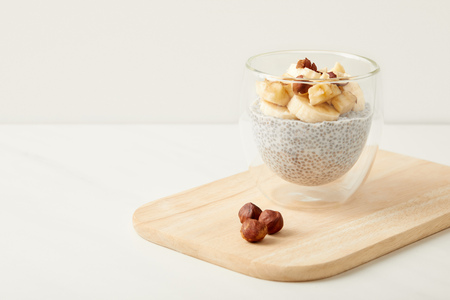 close up view of tasty chia seed pudding with pieces of banana and hazelnuts on wooden cutting board on tabletopの写真素材