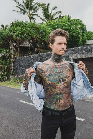 thoughtful tattooed man wearing denim jacket and looking away, bali, indonesiaの写真素材