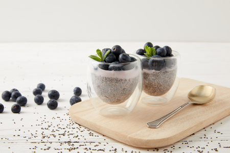 close up view of chia puddings with fresh blueberries and mint on wooden cutting board on white tabletopの写真素材