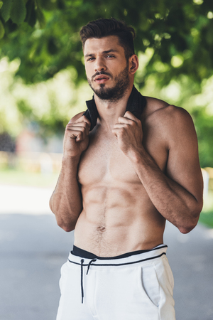 young handsome shirtless sportsman resting after workout with towel on neckの写真素材