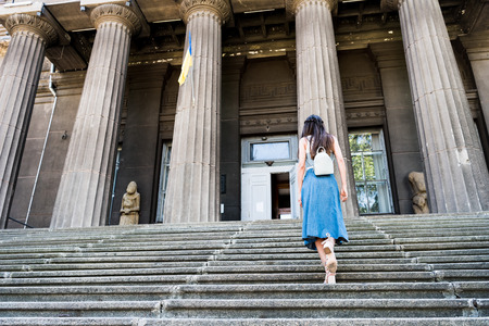 back view of woman in denim skirt with backpack walking up stepsの写真素材