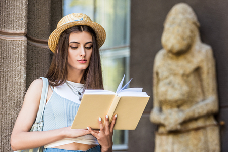 portrait of student in straw hat reading book on streetの写真素材