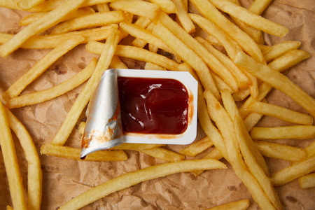 top view of french fries on crumpled paper with container of ketchupの写真素材