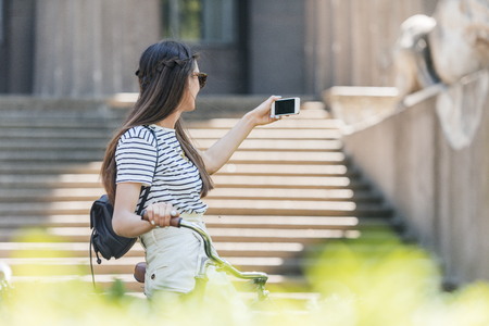 side view of young attractive woman in sunglasses taking selfie on smartphone on streetの写真素材