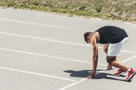 young male sprinter in starting position on running track