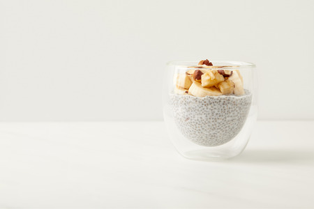 close up view of tasty chia seed pudding with pieces of banana and hazelnuts on white tabletopの写真素材