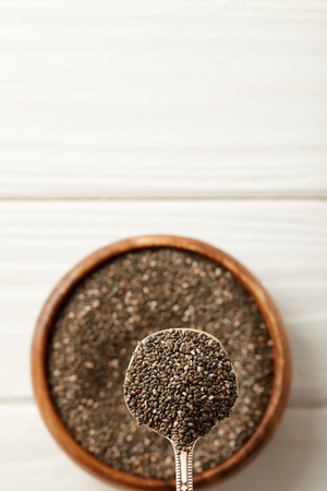 selective focus of chia seeds and spoon in wooden bowl on white surfaceの写真素材