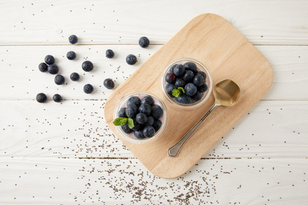 top view of chia puddings with fresh blueberries and mint on wooden cutting board on white surfaceの写真素材