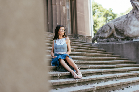 selective focus of girl in eyeglasses sitting on stairs and looking awayの写真素材