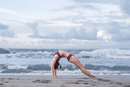 side view of young woman practicing yoga in Wheel pose (Urdhva Dhanurasana) on seashoreの写真素材