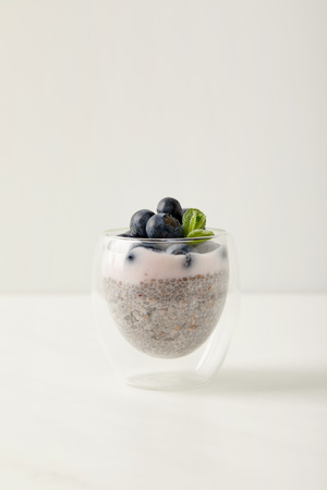 close up view of chia seed pudding with blueberries and mint on white surfaceの写真素材