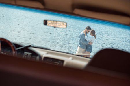 young couple of travelers embracing near the sea, view through carの写真素材