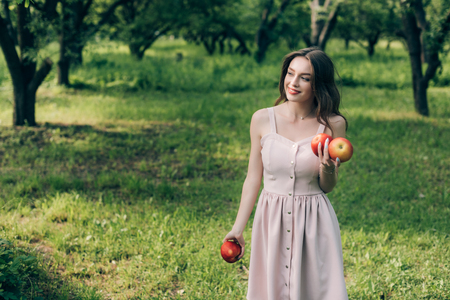 portrait of smiling young woman in dress with ripe apples at countrysideの写真素材