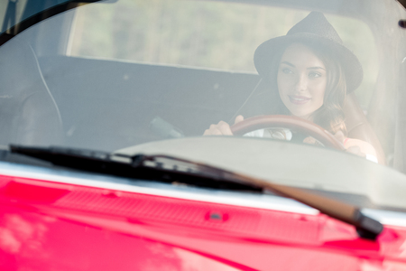 beautiful young woman in hat driving car during road tripの写真素材