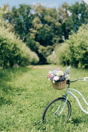 selective focus of retro bicycle with wicker basket full of flowers at countrysideの写真素材