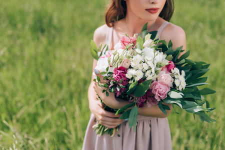 partial view of woman holding bouquet of flowers while standing in field aloneの写真素材