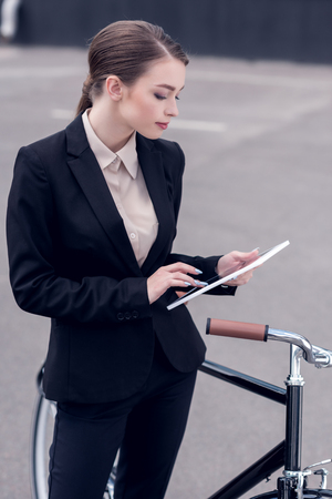 young businesswoman using digital tablet while standing near retro bicycle on streetの写真素材
