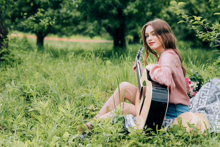 side view of young woman with acoustic guitar resting on blanket with bouquet of flowers in parkの写真素材