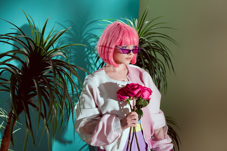 beautiful fashionable female model in pink wig holding roses and looking awayの写真素材